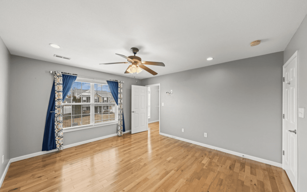 Empty room with hardwood floors, ceiling fan, and large window.