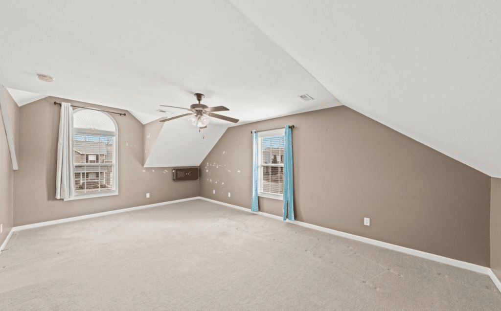 Empty attic room with beige walls and ceiling fan.