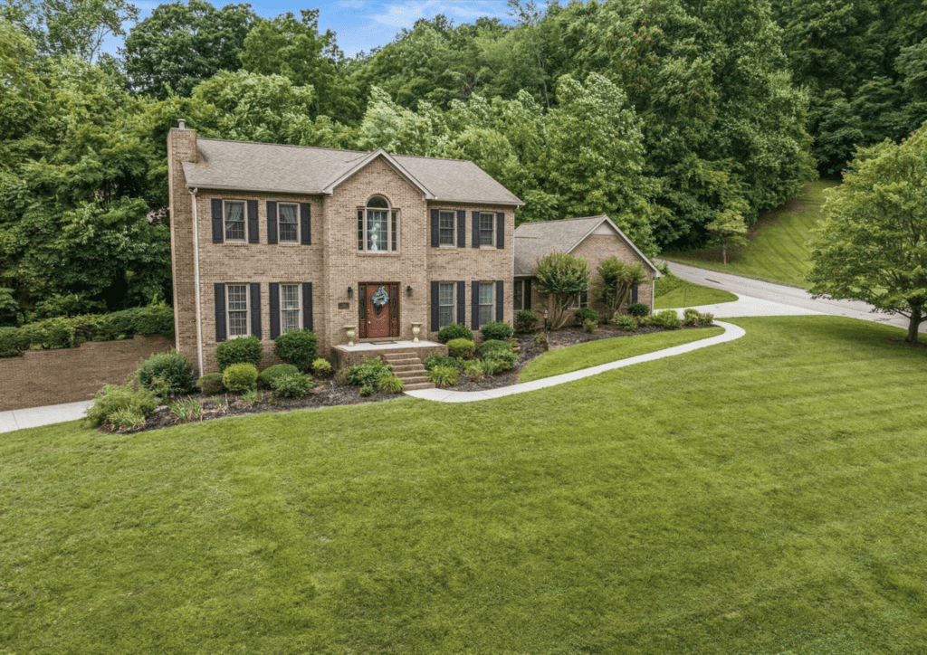 Elegant two-story brick house with a manicured lawn and surrounding greenery.