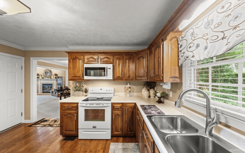 Cozy kitchen with wooden cabinets, white appliances, and a double sink by the window.