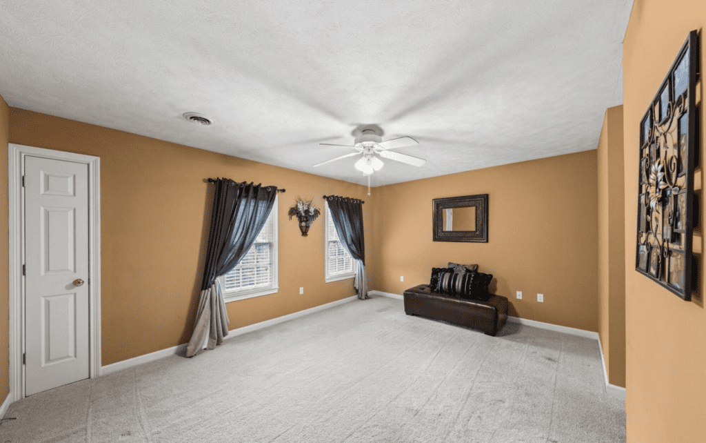Empty room with beige walls, white carpet, and dark curtains.