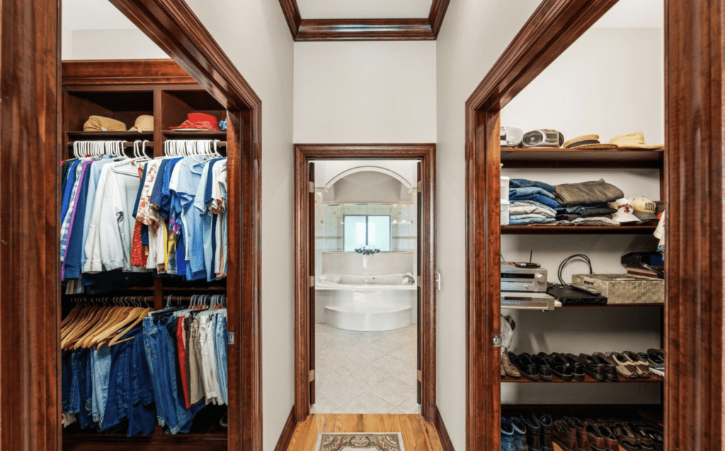 Walkway between two organized closets leading to a bright bathroom.