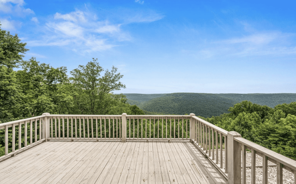 Spacious wooden deck overlooking lush green hills under a clear blue sky.