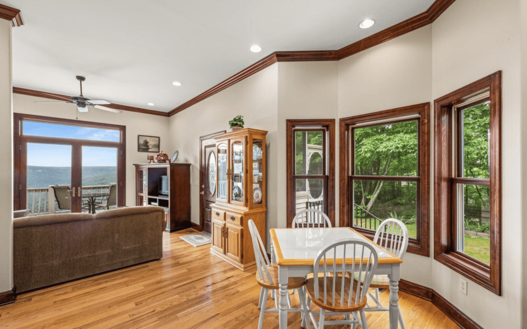 Cozy dining area with wooden floors and large windows overlooking greenery.