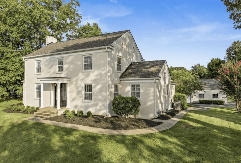 A large beige two-story house with a well-kept lawn and clear blue sky.