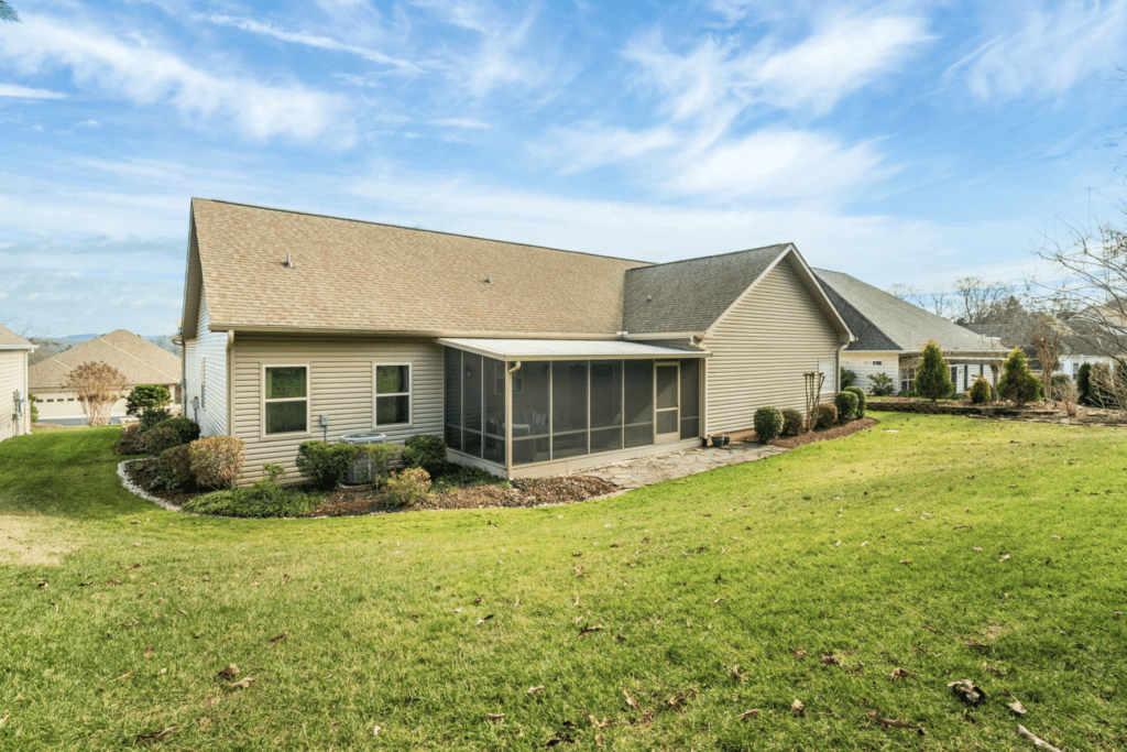 Backyard view of a beige house with a screened porch under a blue sky.