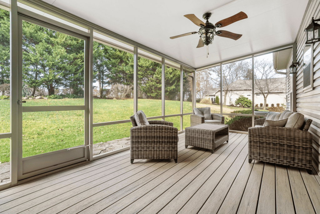 Spacious screened porch with wicker furniture and ceiling fan overlooking a green backyard.
