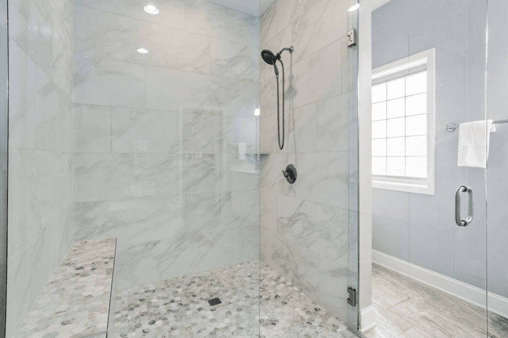 Modern marble shower with glass doors and pebble floor.