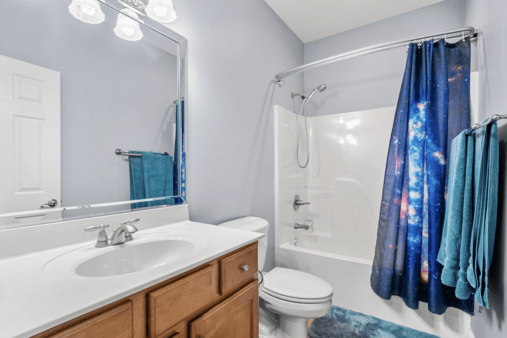 Bright bathroom with wooden vanity, white fixtures, and a blue shower curtain.