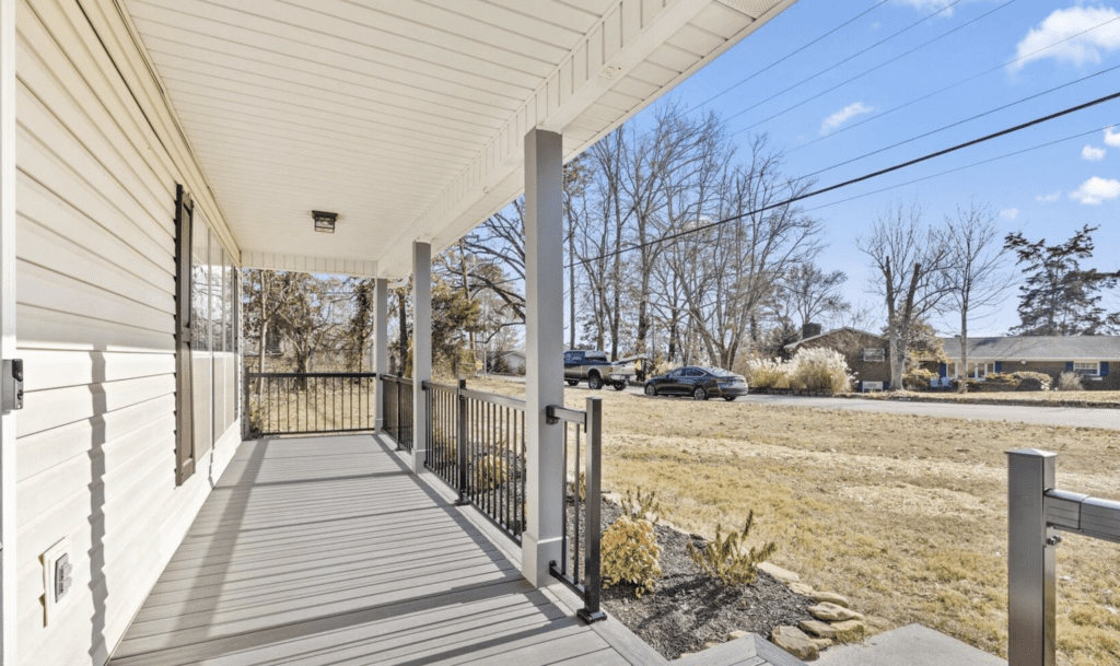 Empty porch with black railing overlooking a grassy yard and road.