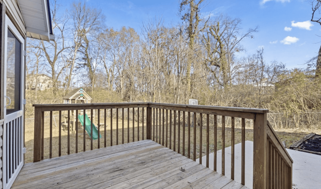 Wooden deck with black railing overlooking leafless trees on a clear day.
