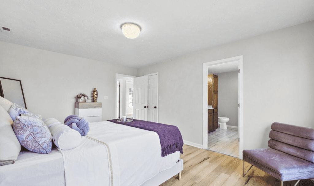 Bright bedroom with white walls, wooden floor, and purple accents.