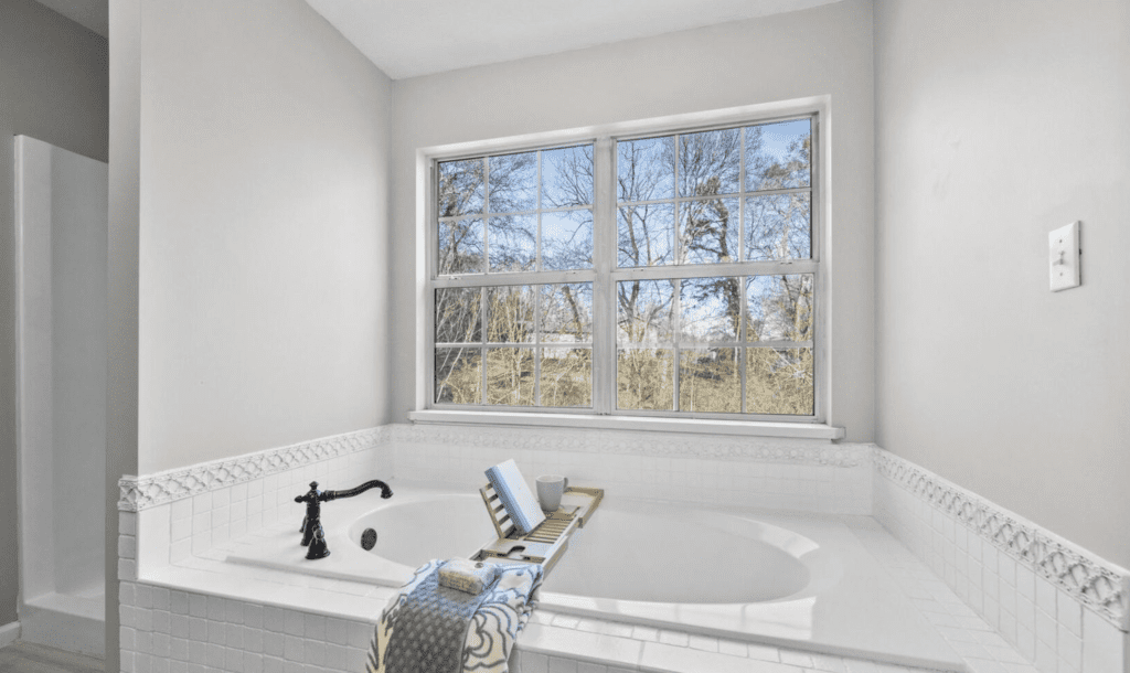 Bright bathroom with a white bathtub and large window overlooking trees.