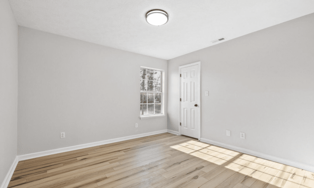 Empty room with wooden floor, white walls, window, and door.
