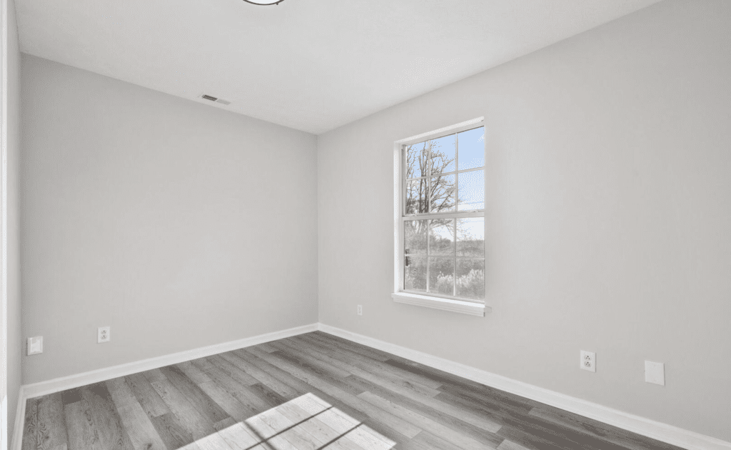 Empty room with gray flooring and a window showing trees outside.