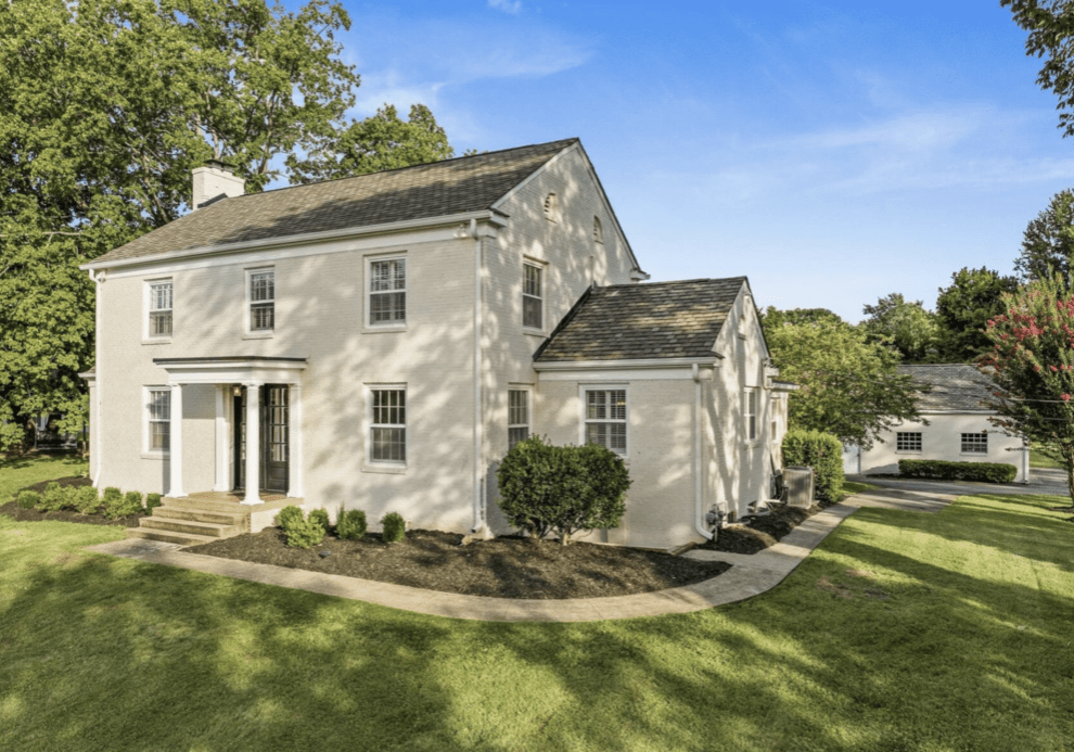 A large beige two-story house with a well-kept lawn and clear blue sky.